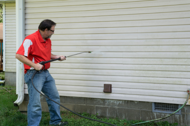 Contractor Using A Pressure Washer To Clean Vinyl Siding